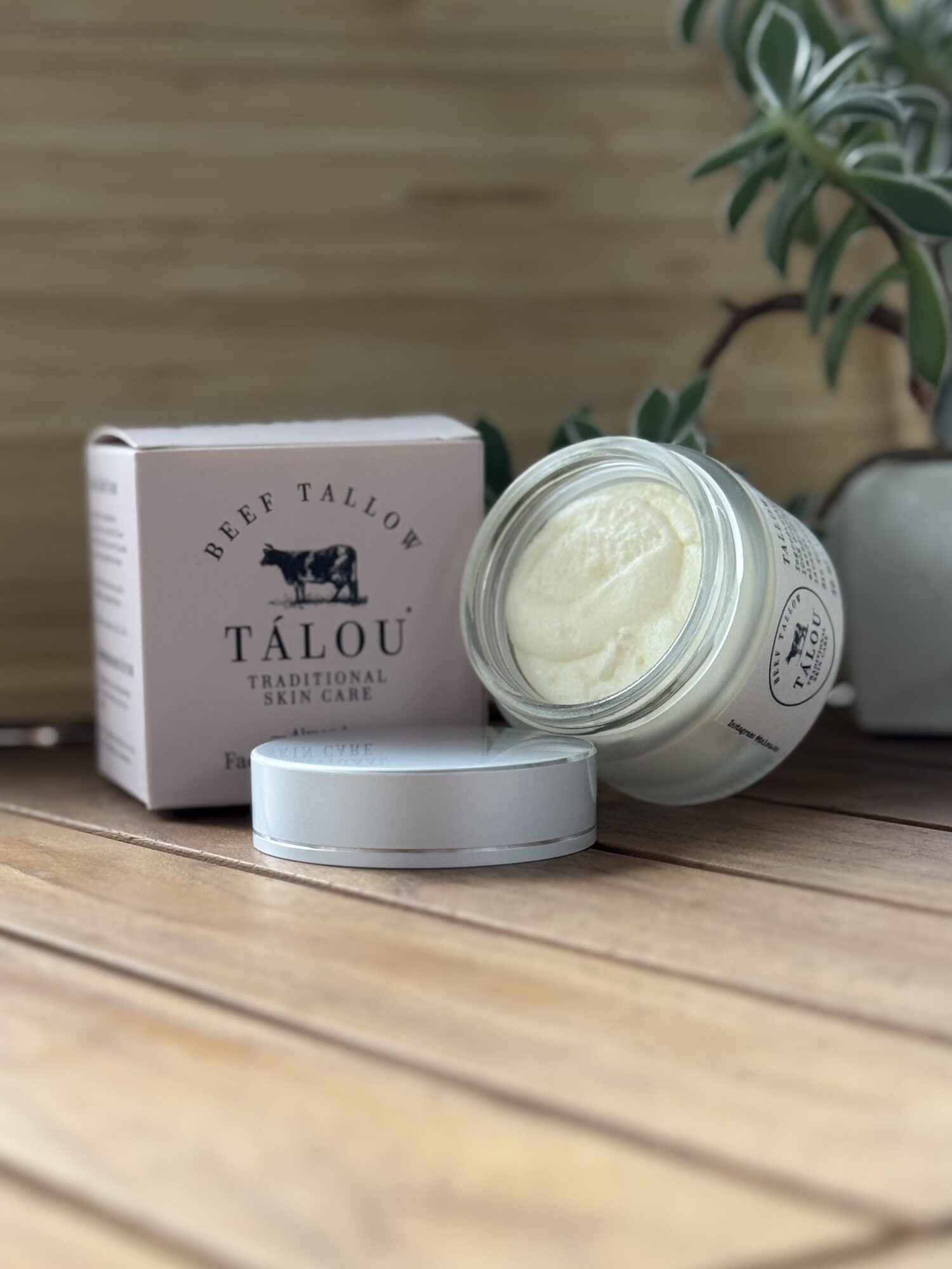 Crema Tálou recién batida junto al frasco abierto, sobre madera con una planta al fondo